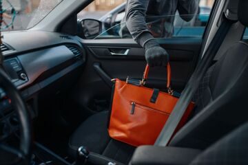 Car robber steals women's handbag, criminal lifestyle, stealing. Hooded male bandit opening vehicle on parking. Auto robbery, automobile crime